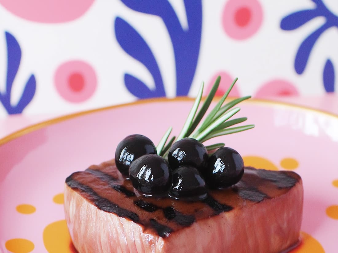 Sliced grilled lamb topped with black olives and rosemary sprigs.