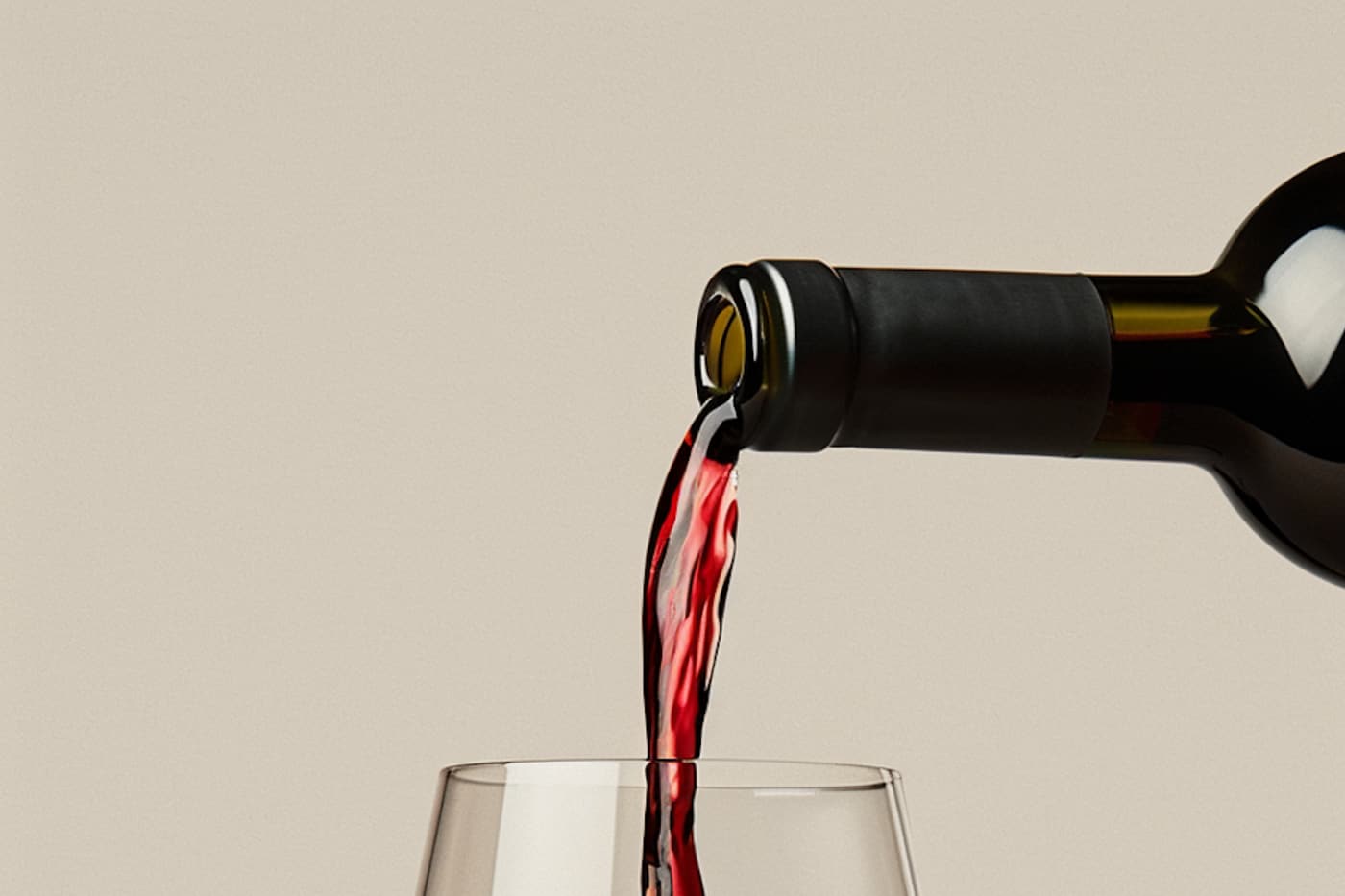 Red wine being poured into a clear glass at a table.